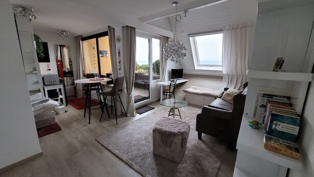 Ein modernes Wohnzimmer mit einer Couch, einem Hocker und einem Essbereich mit Stühlen und einem Tisch.