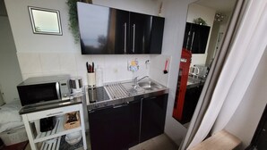Eine kleine Küche mit Mikrowelle, Wasserkocher und Spüle. Über der Arbeitsplatte befinden sich Schränke und darunter ein kleiner Kühlschrank.