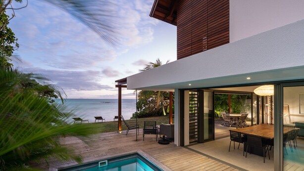 Una casa moderna con piscina, mobiliario exterior y vistas al océano.