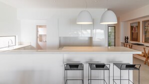 Una cocina moderna con una isla central, taburetes de bar, iluminación colgante y vistas al exterior.