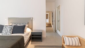 Un dormitorio moderno con una cama, mesitas de noche, una silla y un pasillo que conduce a una puerta.