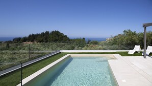 Une piscine rectangulaire à l’eau claire, entourée d’une pelouse bien entretenue et d’un espace détente avec des chaises longues blanches.