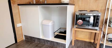A compact kitchenette with a built-in stove, a small sink, and a white trash bin.