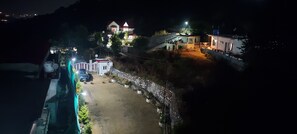 A nighttime view of a residential area with houses, a paved road, and a small white building with a red roof. - LakeBreeze By Sunrise (Nainital)