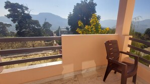 A balcony with a chair, a view of mountains, and a tree with yellow flowers. - LakeBreeze By Sunrise (Nainital)
