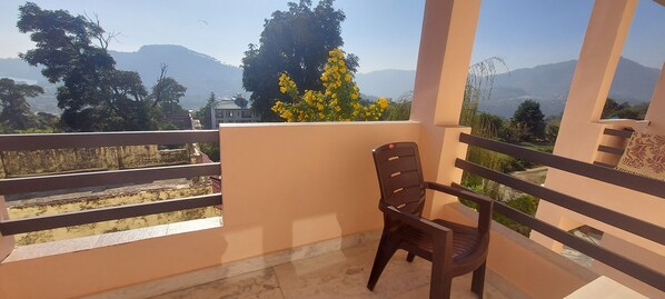 A balcony with a chair, a view of mountains, and a tree with yellow flowers. - LakeBreeze By Sunrise (Nainital)
