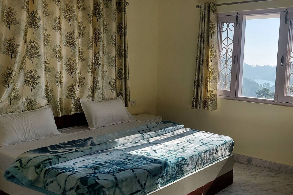 A bedroom with a bed, curtains, a window, and a view of the outdoors.