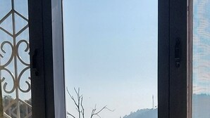 A room with a window overlooking a landscape with hills and a body of water. - LakeBreeze By Sunrise (Nainital)