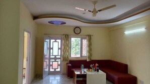 A living room with a red sofa, a white coffee table, a ceiling fan, and a window with curtains. - LakeBreeze By Sunrise (Nainital)
