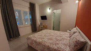 Een slaapkamer met een bed, bureau, stoel, televisie en een raam met gordijnen.