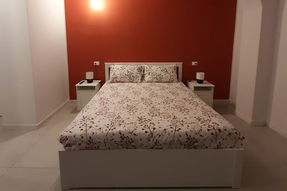 Een slaapkamer met een bed, twee nachtkastjes en een wandlamp.