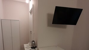 Een kleine, witte kamer met een bureau, stoel en een televisie aan de muur.