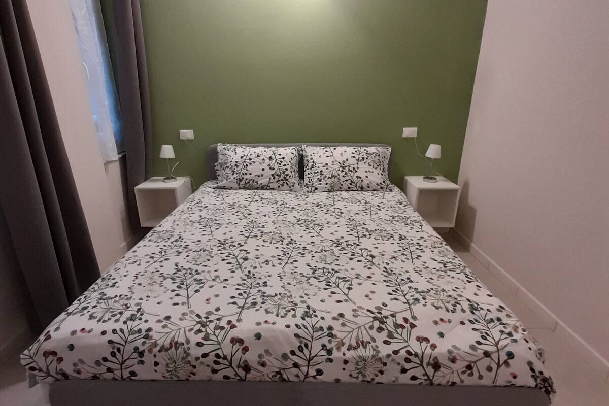Een slaapkamer met een bloemenbedekker, twee bedlampen en een wandlamp.