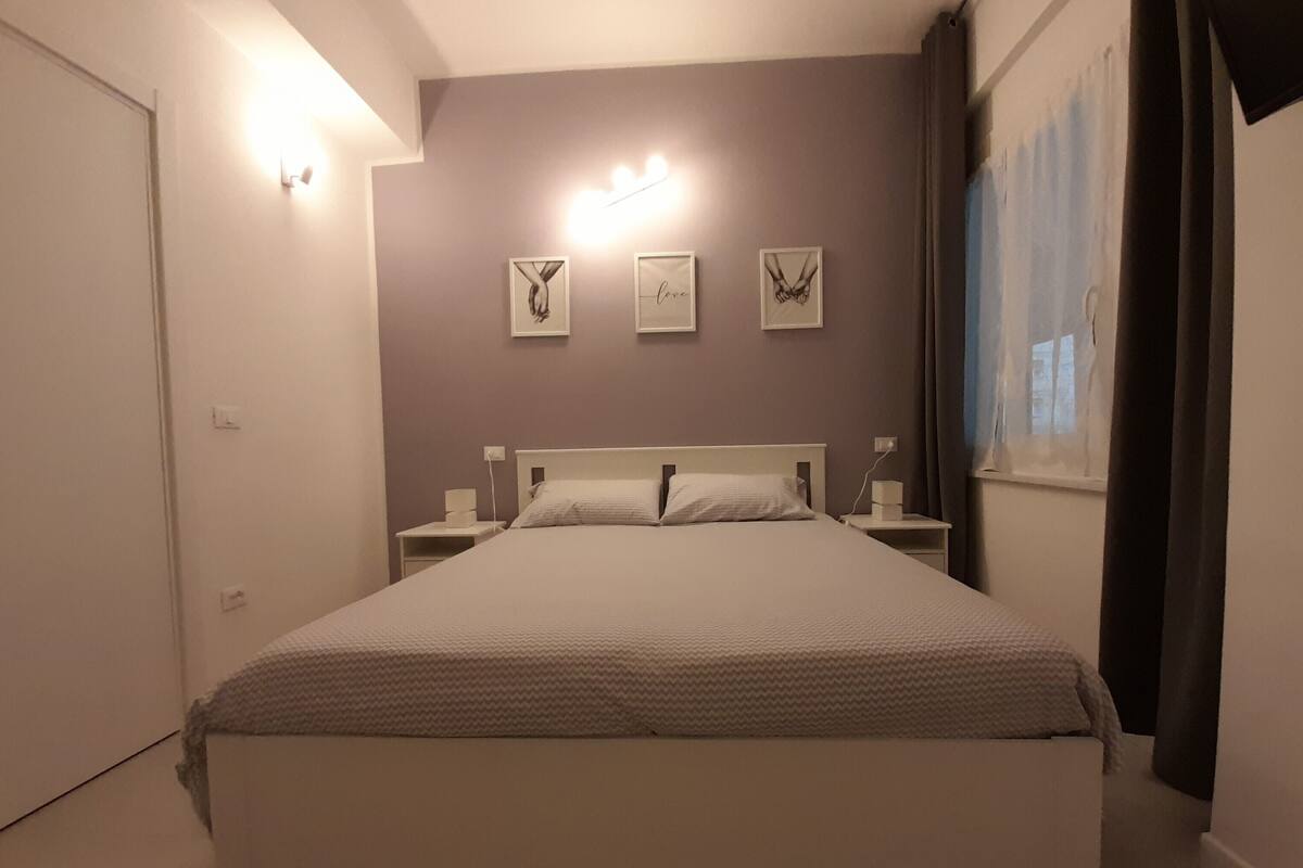 Een slaapkamer met een groot bed, nachtkastjes, een wandlamp en drie ingelijste foto’s.