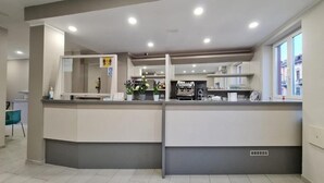 A reception area with a counter, a small seating area, and a view of the street through large windows. - Hotel City 20 (Milan)