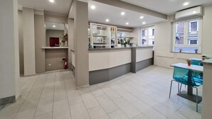 A modern kitchen with white cabinets, a central island, and a dining area with a blue chair. - Hotel City 20 (Milan)
