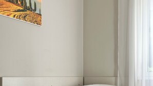 A modern living room with a white sofa, a white armchair, a glass coffee table with a vase of flowers, and a painting of a landscape on the wall. - Hotel City 20 (Milan)