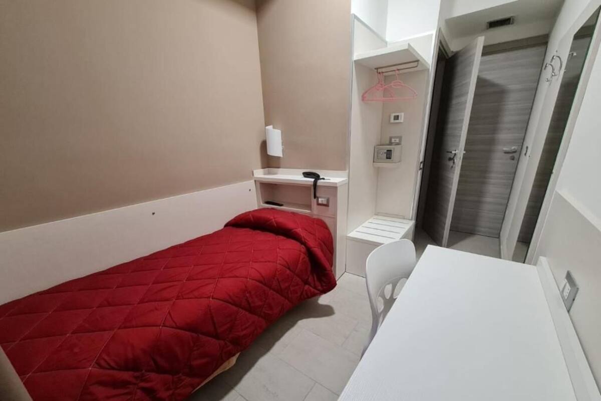 A small, compact room with a single bed, a desk, a chair, and a walk-in closet.