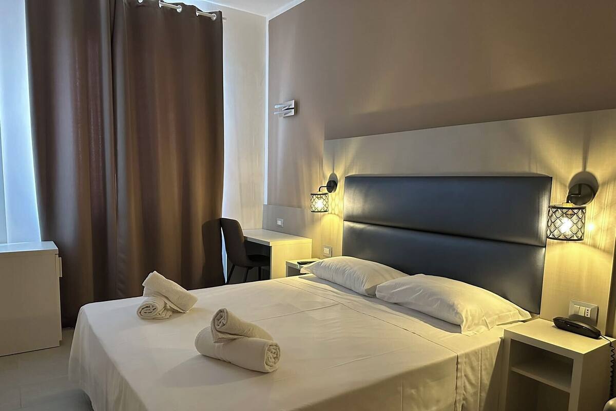 A hotel room with a large bed, two bedside tables, a desk, and a chair.
