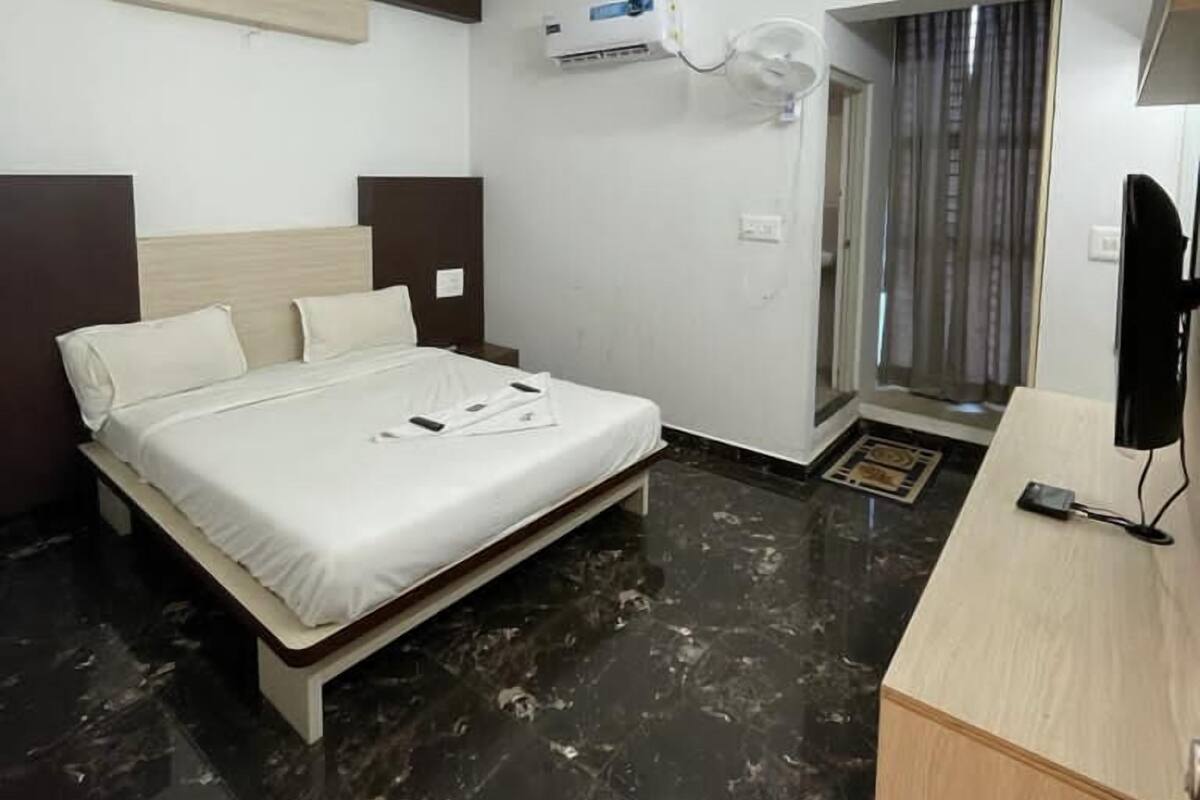 A hotel room with a bed, a desk, an air conditioning unit, and a television.