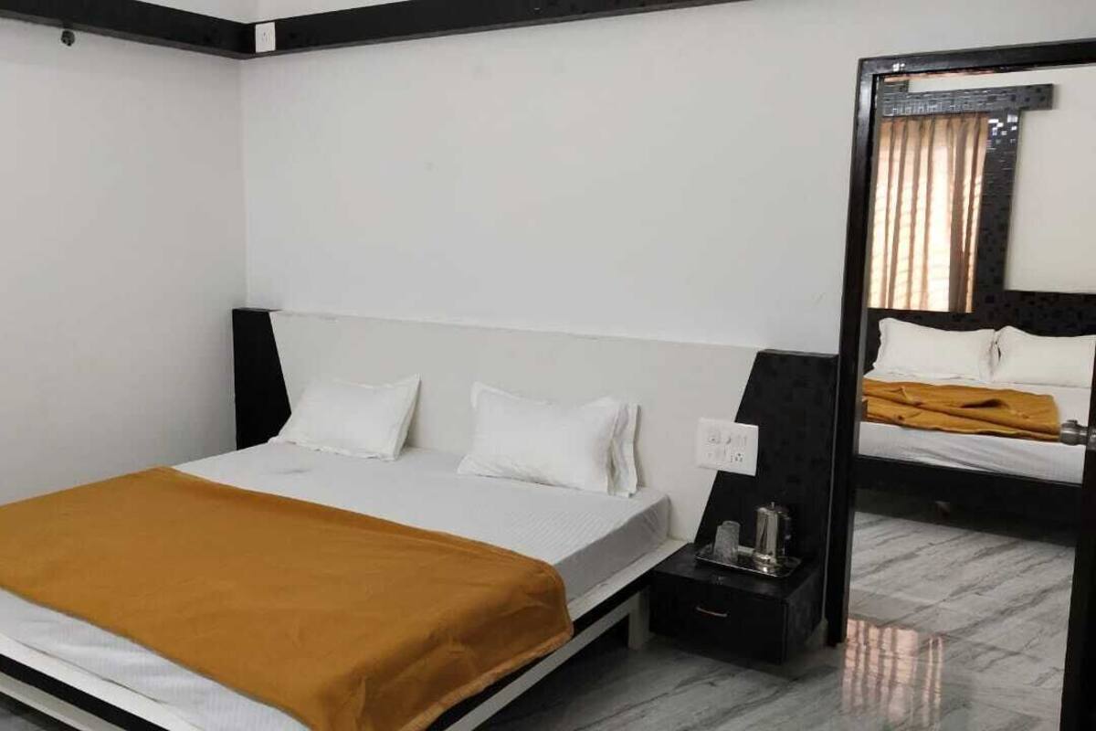 A hotel room with a bed, a nightstand, a mirror, and a window with curtains.
