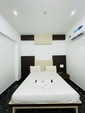 A single bed in a room with a dark headboard, a small bedside table, and a wall-mounted air conditioning unit. - iROOMZ S Silver Suites (Mysore)