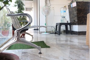 A reception area with a marble floor, a reception desk, a water dispenser, a fan, and a bench. - iROOMZ S Silver Suites (Mysore)