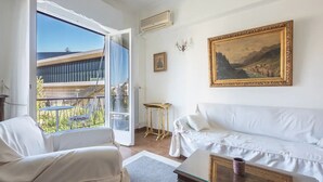 A room with a white sofa, a small table, and a balcony with a view of buildings and greenery. - Classic Athenean Apartment at Acropolis Museum & Metro (Athens)