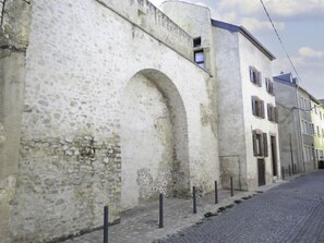 A cobblestone street with a historic stone building featuring an arched entrance and a small window above it.