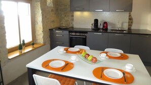 Une cuisine moderne avec des meubles gris, une cuisinière noire et un pare-feu en carreaux. On y trouve une table à manger avec des sets de table orange et des assiettes blanches.