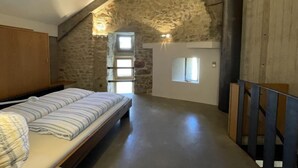 Une chambre avec un plafond en pente, des murs en pierre, un lit en bois et une petite fenêtre.