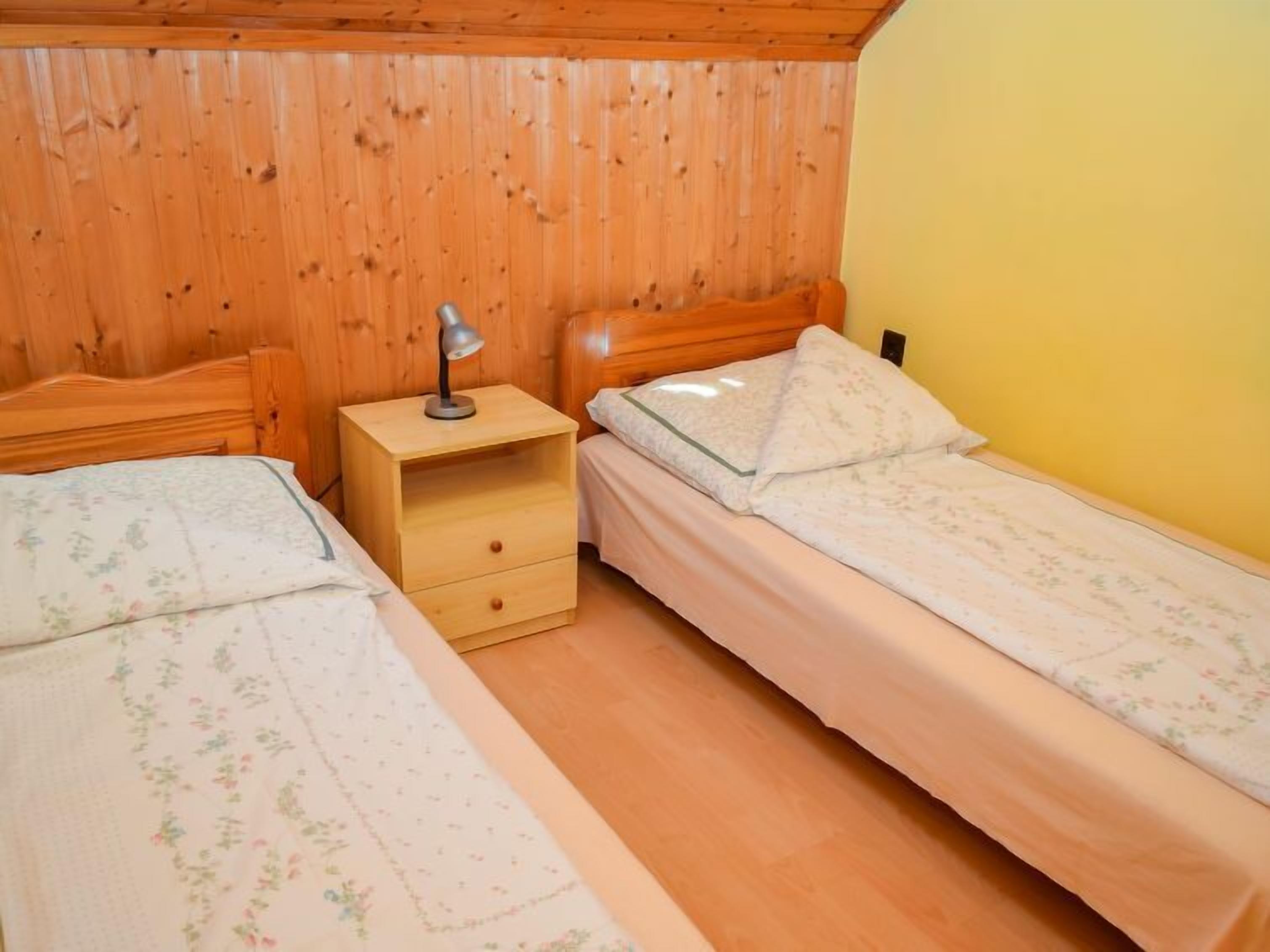 A room with two single beds, wooden headboards, a nightstand with a lamp, and a yellow wall.