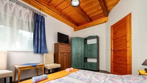 Ein Schlafzimmer mit Holzboden, einem Bett mit bunter Steppdecke, einem Schreibtisch mit Stuhl, einem Kleiderschrank und einem Fernseher.