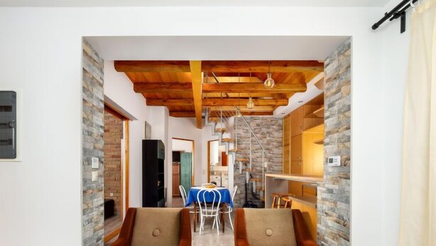 Ein modernes Interieur mit freiliegenden Holzbalken, Steinwänden und einem Essbereich mit blauer Tischdecke.