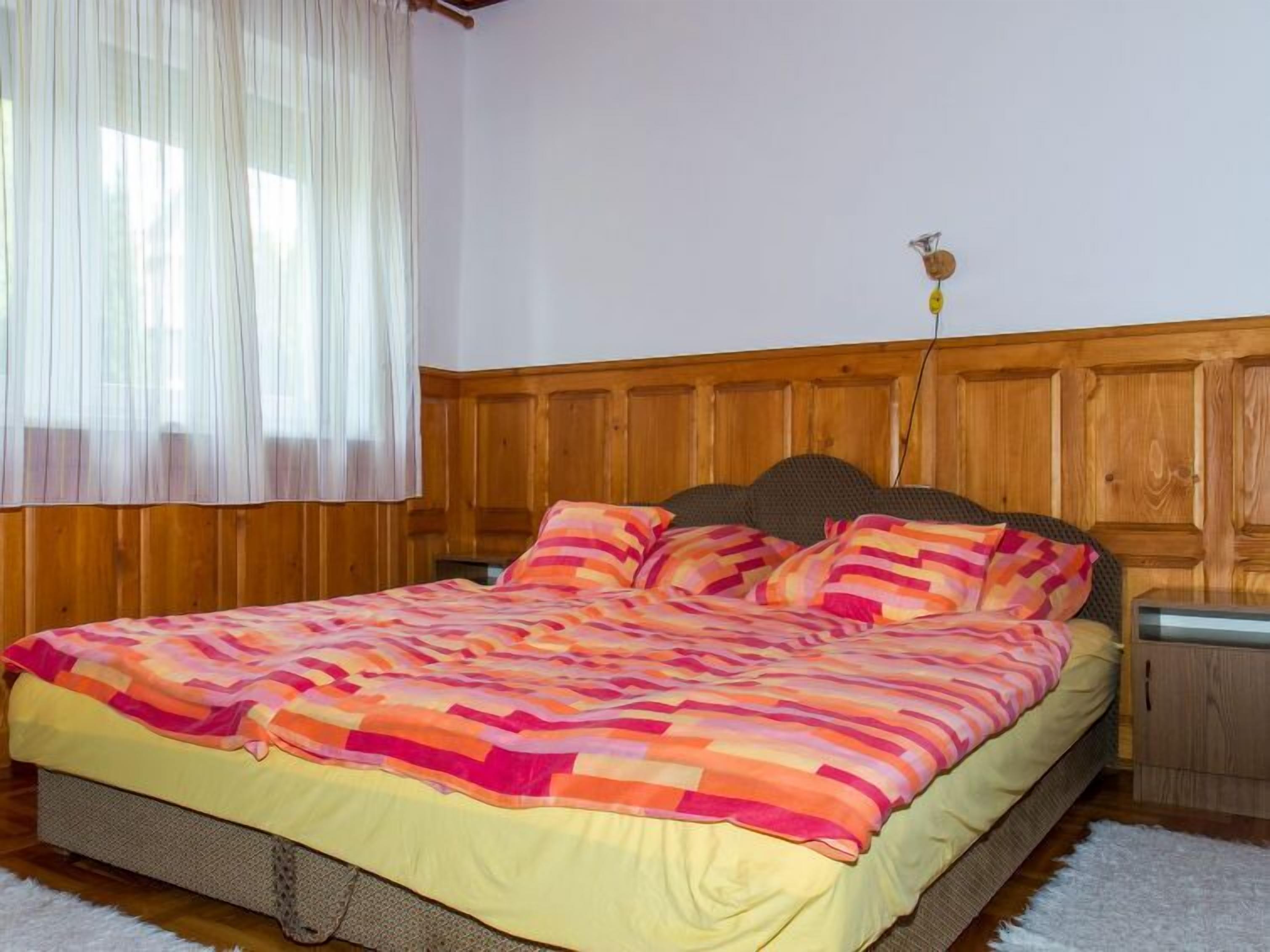 Une chambre à coucher avec une tête de lit en bois, un lit recouvert d’une courtepointe à rayures colorées et une fenêtre ornée de rideaux légers.