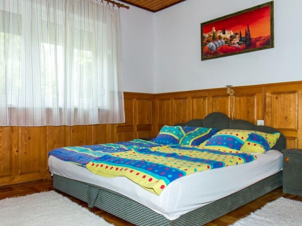 A bedroom with a wooden headboard, a colorful bedspread, and a painting on the wall. - Vacation home Marie by Interhome (Balatonmariafurdo)
