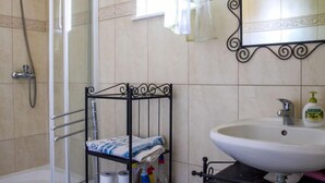 Une salle de bain équipée d’une douche, de papier toilette, de produits de nettoyage et d’un lavabo.