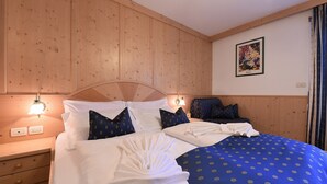 A hotel room with a wooden headboard, two beds with white and blue bedding, a nightstand with a lamp, and a wall-mounted poster. - Top Located Alpin-Residence Amadeus*** Luxury Alpine GEM for 2 Pax (Seis)