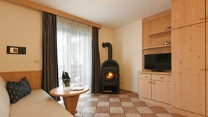 A cozy room with a sofa, a small table with a bottle and glasses, a fireplace, a TV, and wooden cabinets. - Top Located Alpin-Residence Amadeus*** Luxury Alpine GEM for 2 Pax (Seis)