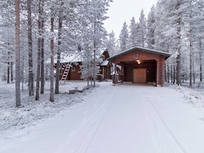 A log cabin with a wooden porch and a ladder leading to a loft, surrounded by snow-covered trees. - Petsankolo by Interhome (Pelkosenniemi)