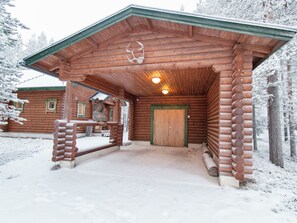 A wooden cabin with a covered entrance, a bear statue, and a snow-covered landscape.