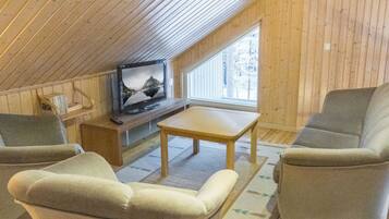 Une pièce mansardée chaleureuse, équipée d’une télévision, d’une table en bois et de deux fauteuils.