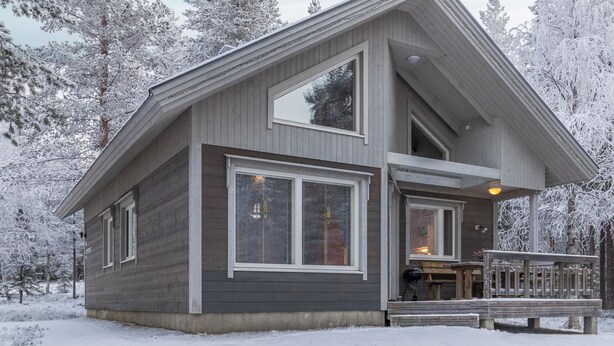 Een modern chalet met twee verdiepingen, grote ramen, een overdekte veranda en een terras.