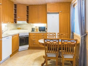 Een kleine keuken met houten kastjes, een fornuis, een magnetron en een eettafel met stoelen.