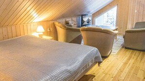 Een knus zolderkamertje met een houten schuine dak, een bed, twee fauteuils, een kleine tafel en een televisie.