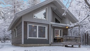 Een tweelaags huis met een ruime veranda en een terras, omgeven door met sneeuw bedekte bomen.