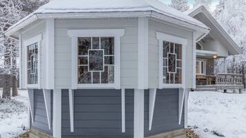 A snow-covered gazebo with a dark siding exterior and white trim.