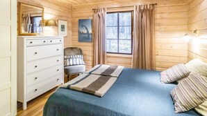 A cozy wooden cabin bedroom with a bed, dresser, and a window with curtains.