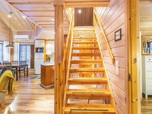Un interior de madera con una escalera central, una zona de cocina y un comedor.