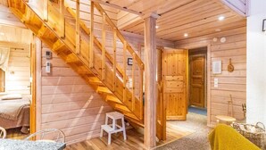 A wooden interior with a staircase, a small stool, a bed, and a dining area.